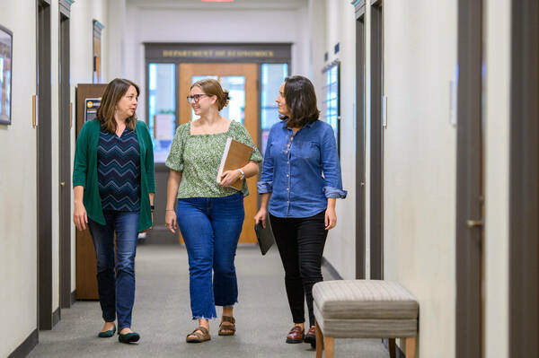 Three women walking in a hallway, talking to one another.