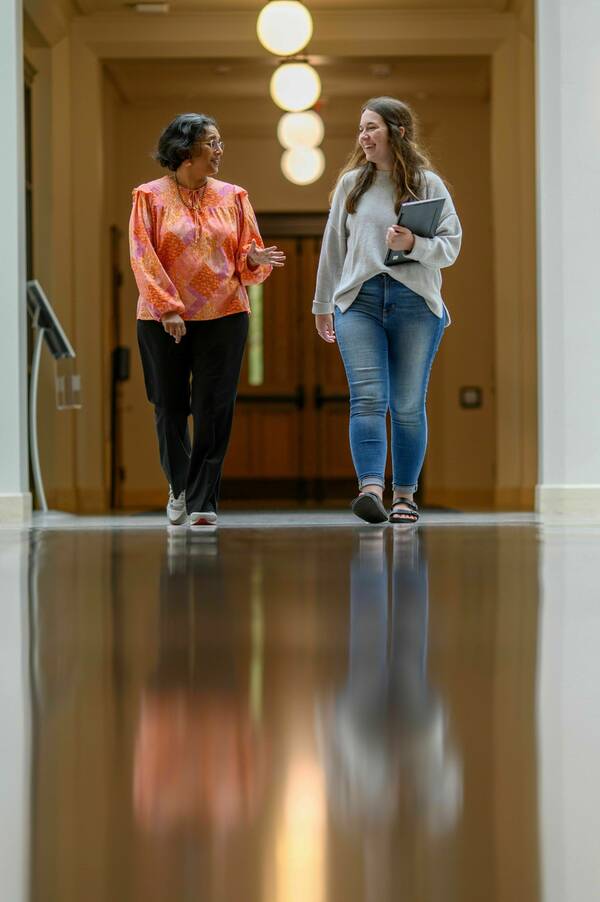 A student and professor, engaged in a conversation, walk the halls